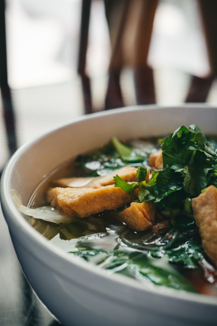A mouthwatering close-up of Vietnamese pho with fresh herbs and vegetables in a white bowl.