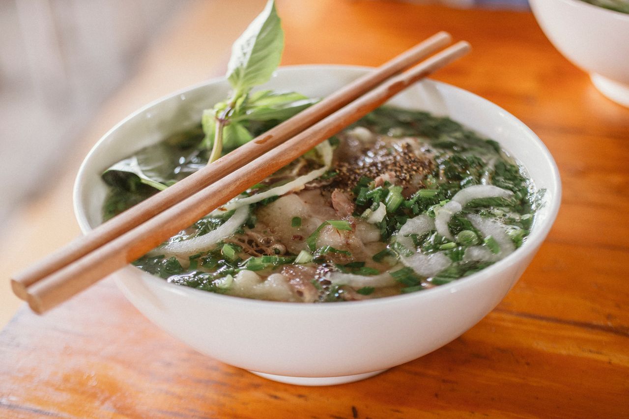 Delicious Vietnamese pho with fresh herbs and beef in a ceramic bowl, served with chopsticks.
