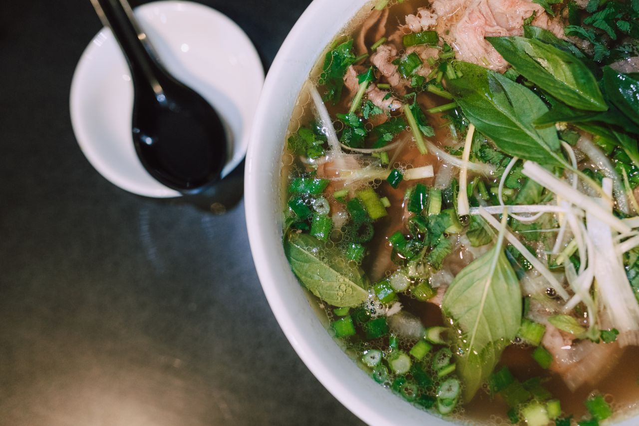 Delicious, traditional Vietnamese pho soup with fresh herbs and toppings in a white bowl.
