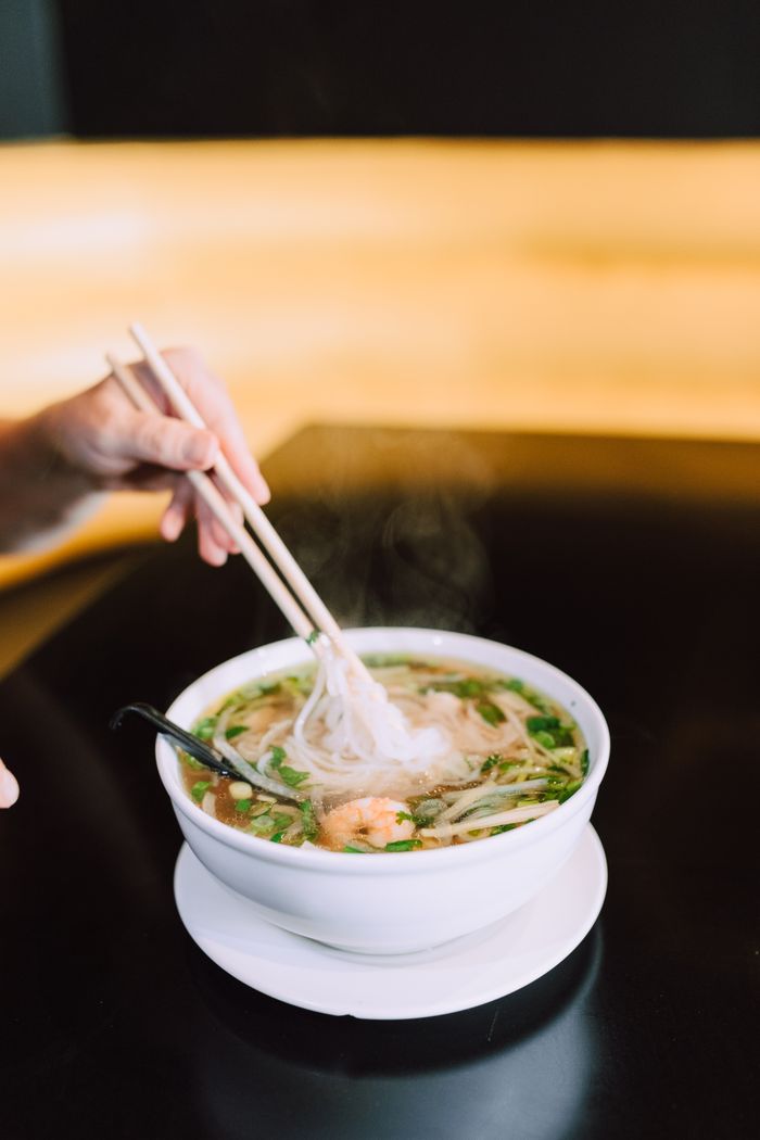 A steaming bowl of Vietnamese pho with a hand using chopsticks.